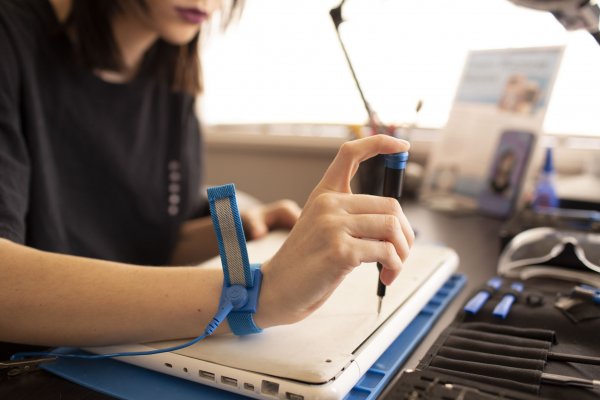 Woman with an anti-static wrist strap opens a laptop computer with an iFixit screwdriver